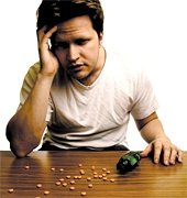 Man with a headache sitting at table with pain pills scattered over its surface. - Copyright – Stock Photo / Register Mark