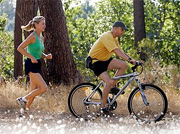 A woman jogging behind a man who is mountain biking. - Copyright – Stock Photo / Register Mark